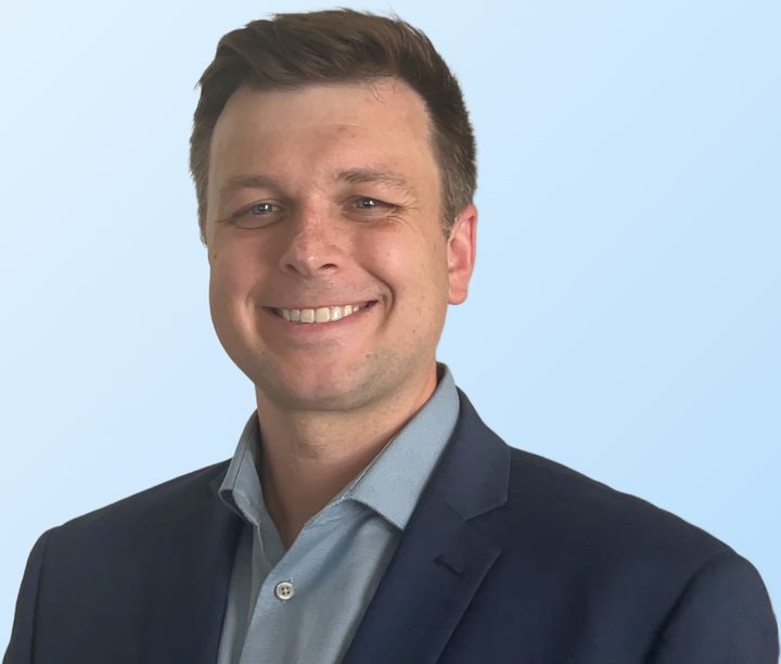 Portrait of Eric Iverson, founder of Montage Neuroscience, smiling, in a navy blazer and light blue shirt